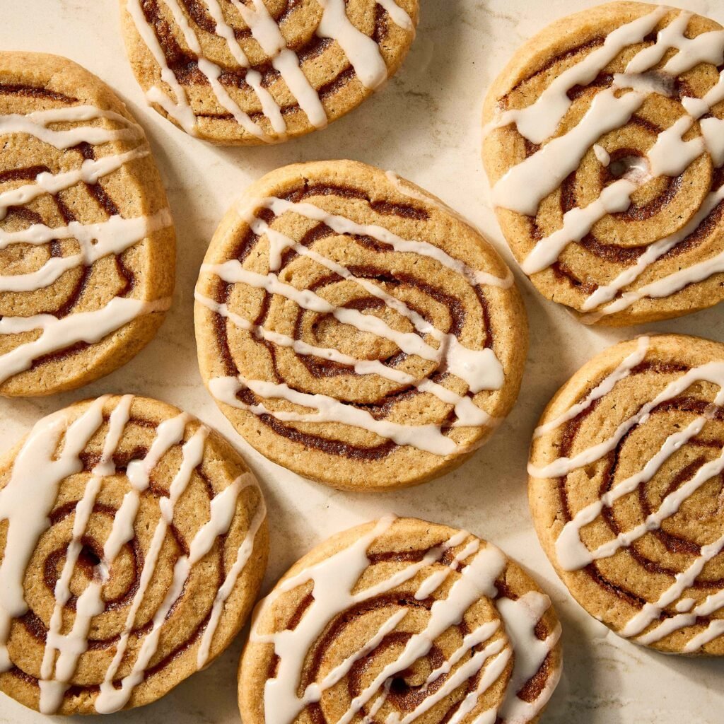 Biscoitos em formato espiral com recheio de canela e cobertura de glacê branco.
