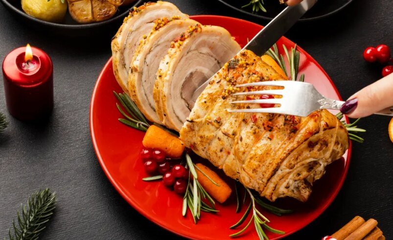 Lombo fatiado em prato vermelho com cenouras, alecrim e decoração natalina.