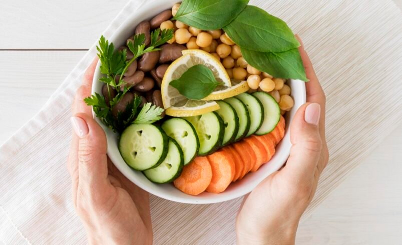 Mãos segurando uma tigela com salada de legumes frescos e ervas.