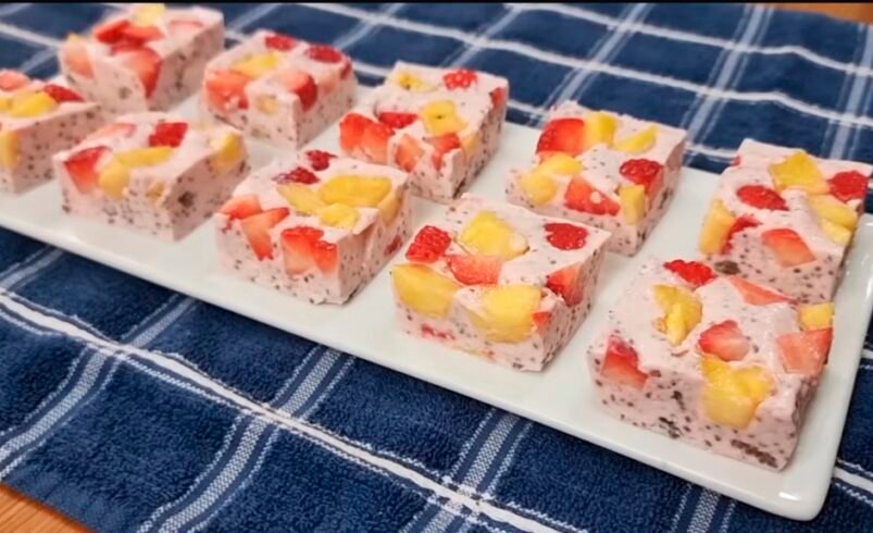 Cubos de sobremesa com frutas e chia dispostos em um prato branco sobre toalha azul.