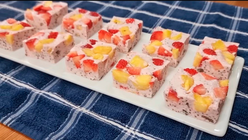 Cubos de sobremesa com frutas e chia dispostos em um prato branco sobre toalha azul.