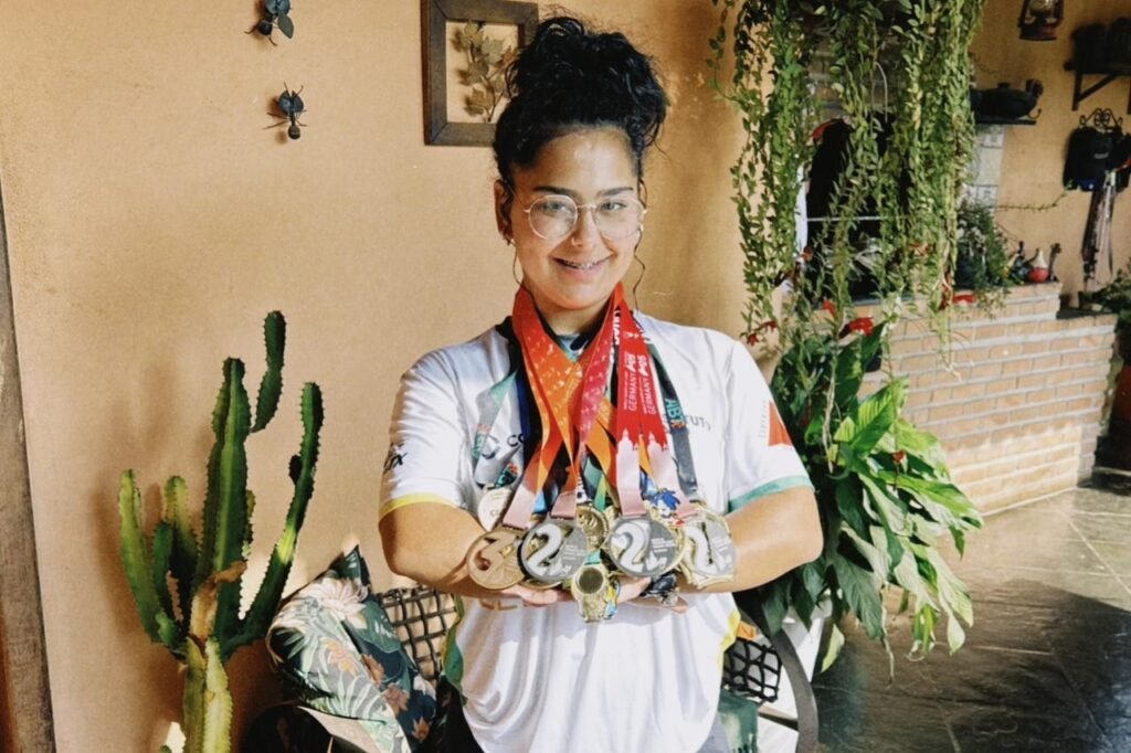 Pessoa segurando medalhas em ambiente com plantas e decoração rústica.