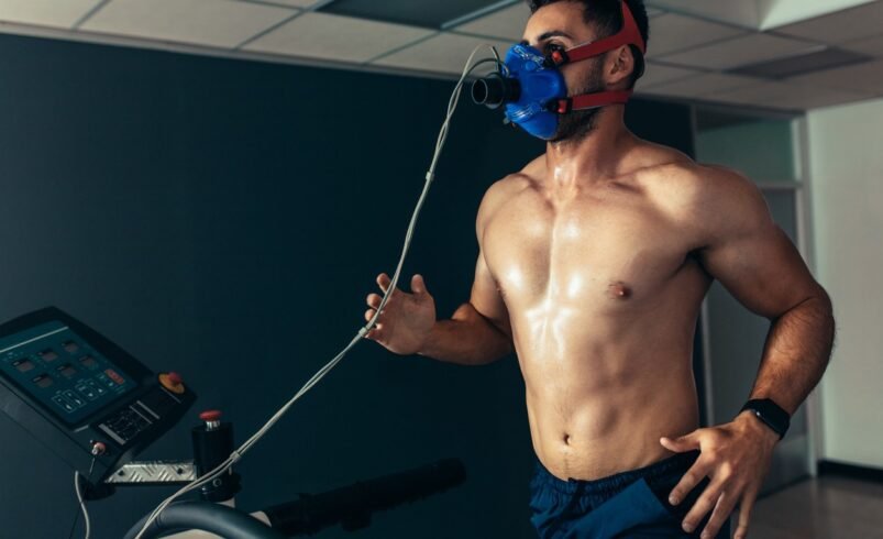 Homem correndo em esteira, usando máscara de oxigênio, em ambiente interno.