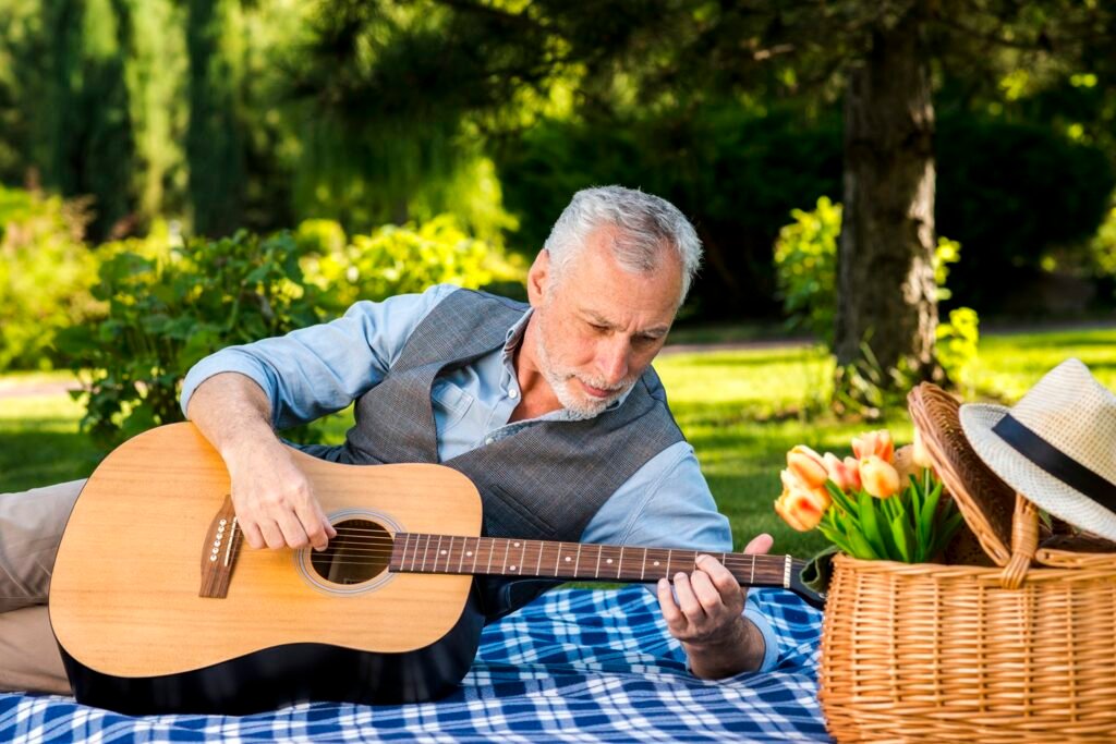 Pessoa tocando violão em piquenique com cesta e flores no gramado.