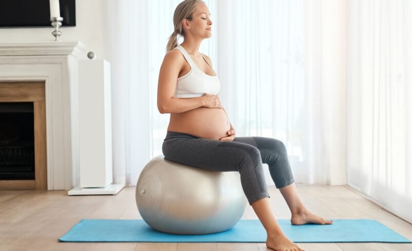 Gestante sentada em bola de pilates em ambiente iluminado.