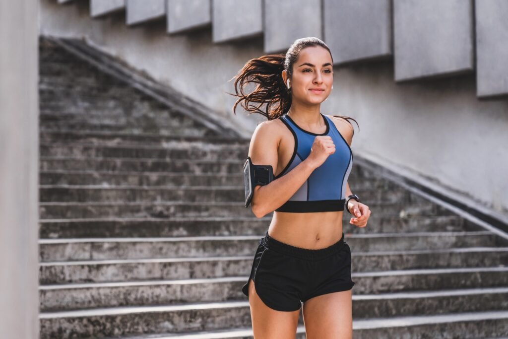 Mulher usando top azul e shorts preto correndo em escadaria.