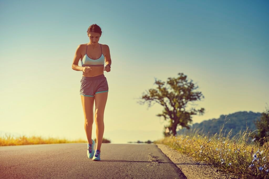 Mulher praticando corrida em estrada sob céu claro ao amanhecer.