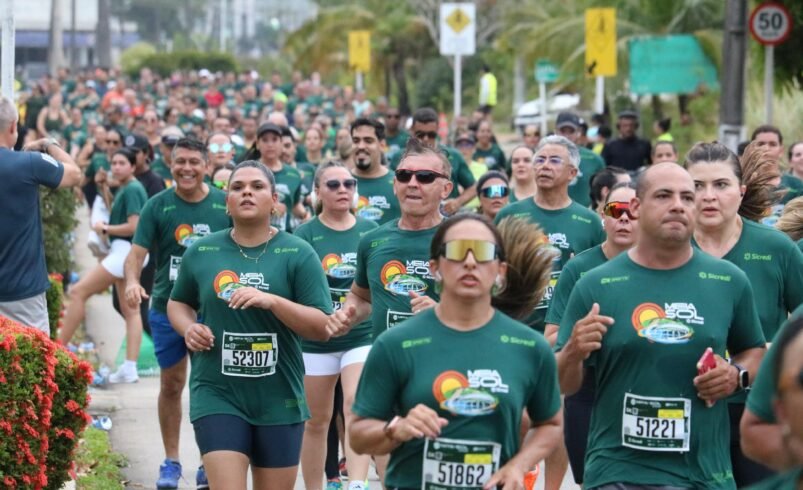 Grupo de corredores participando de corrida em via arborizada.