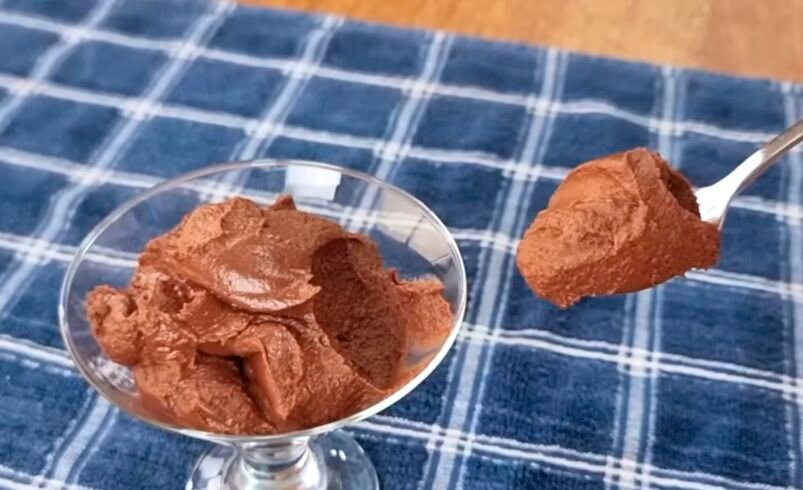 Taça de mousse de chocolate sobre toalha azul, com colher servindo.