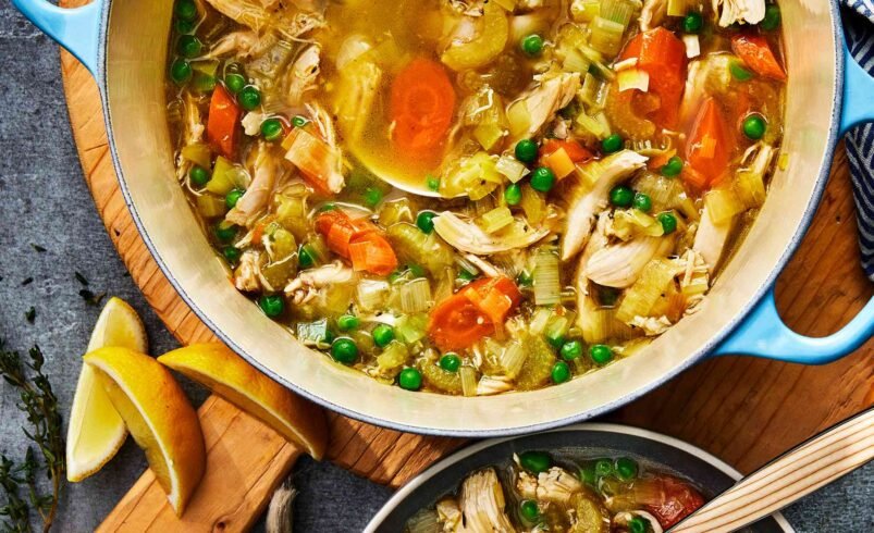 Panela com ensopado de frango, legumes coloridos e colher de servir.