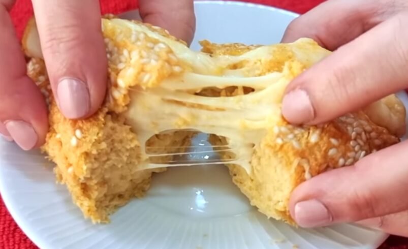 Mãos abrindo pão de queijo dourado com queijo derretido se esticando.