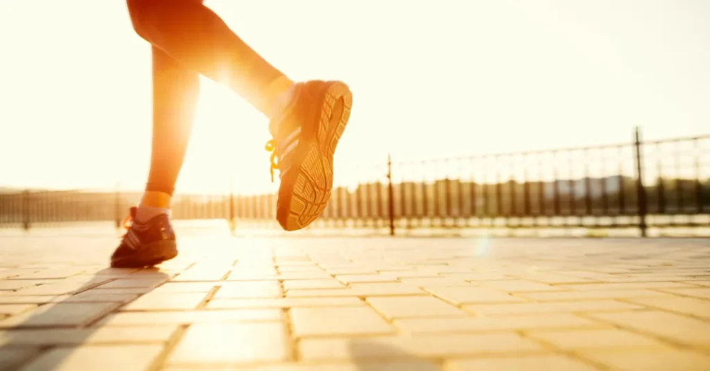 Pessoa caminhando ao amanhecer em uma calçada pavimentada iluminada pelo sol.