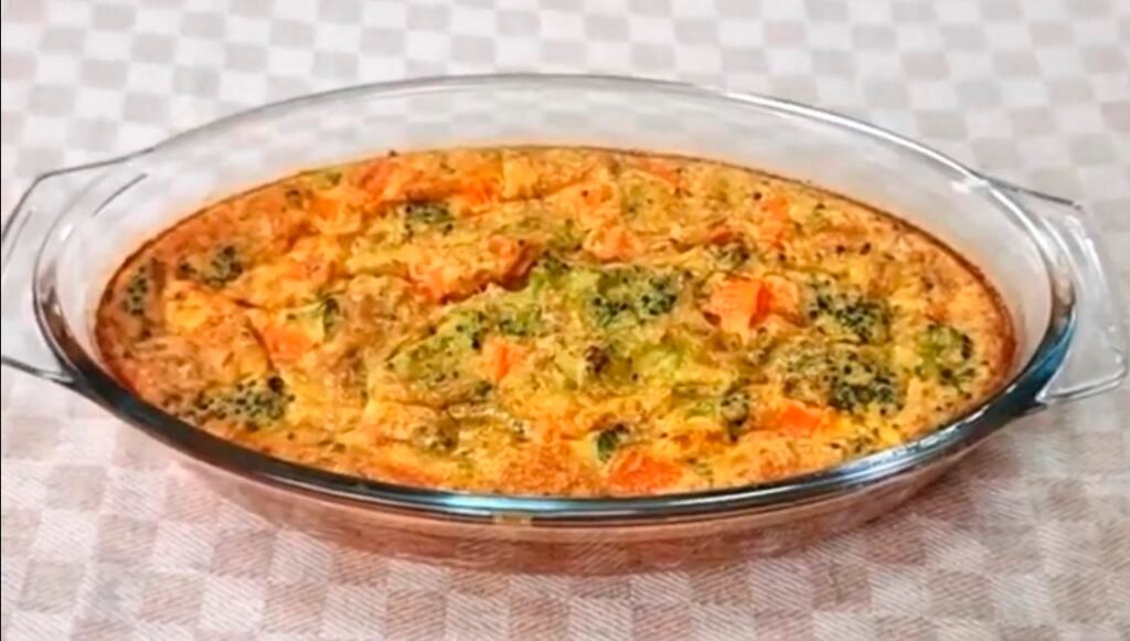 Torta salgada de legumes assada em travessa de vidro sobre toalha xadrez.