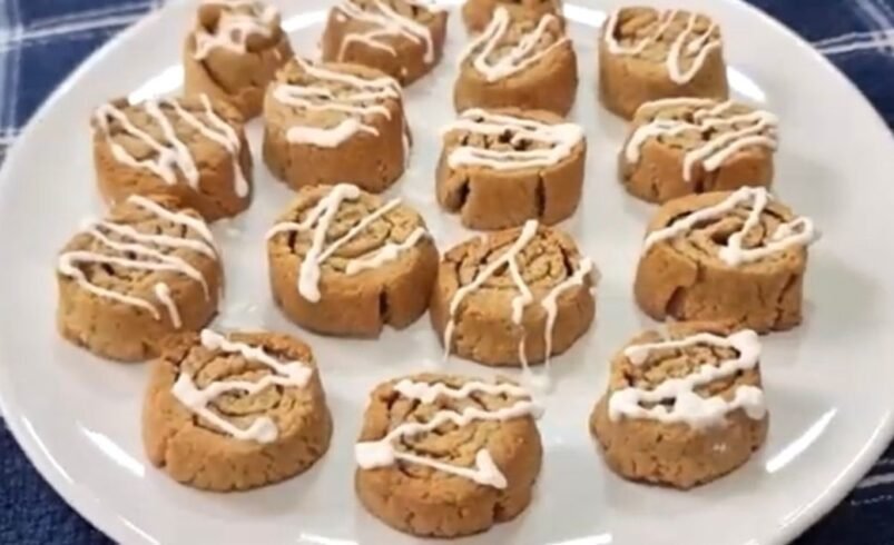 Biscoitos caseiros com glacê dispostos em um prato branco sobre toalha azul.