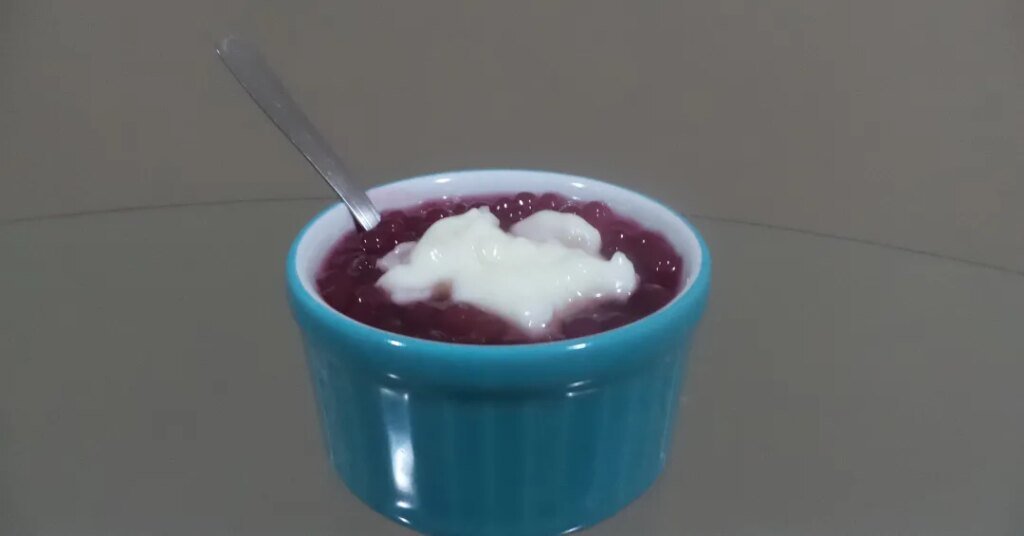 Tigela azul com sobremesa de tapioca, cobertura branca e colher.