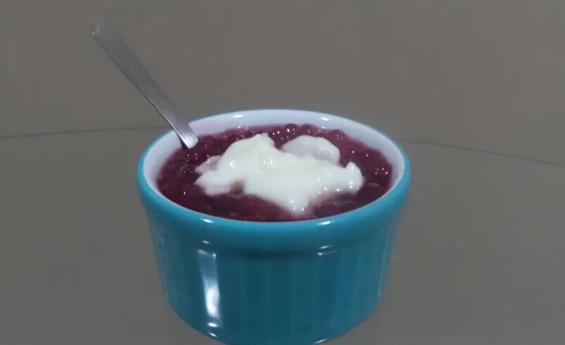Tigela azul com sobremesa de tapioca, cobertura branca e colher.
