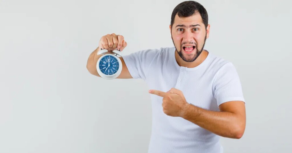 Síndrome da pressa: conheça causas, sintomas e tratamento 1 Pessoa apontando para um relógio analógico azul em fundo branco.