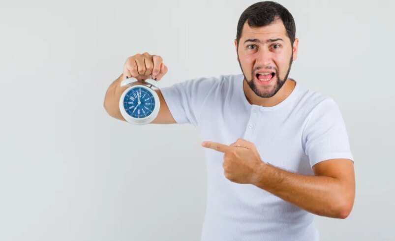 Pessoa apontando para um relógio analógico azul em fundo branco.