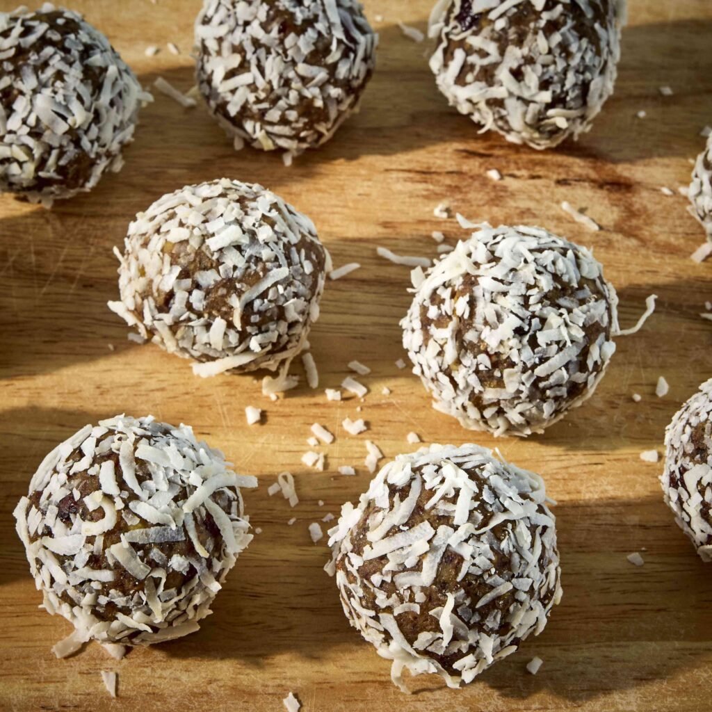 Vários brigadeiros cobertos com coco ralado sobre superfície de madeira.