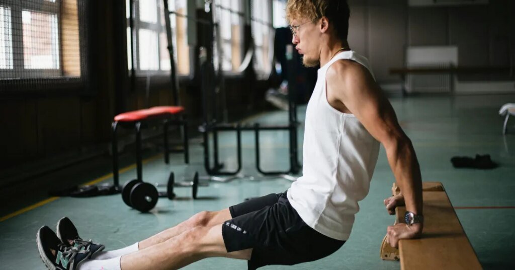 Tríceps banco: conheça esse exercício que define os braços 1 Pessoa realizando exercício de tríceps em barra fixa em ambiente de academia.