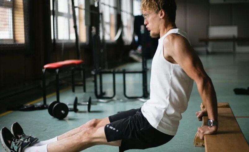 Pessoa realizando exercício de tríceps em barra fixa em ambiente de academia.
