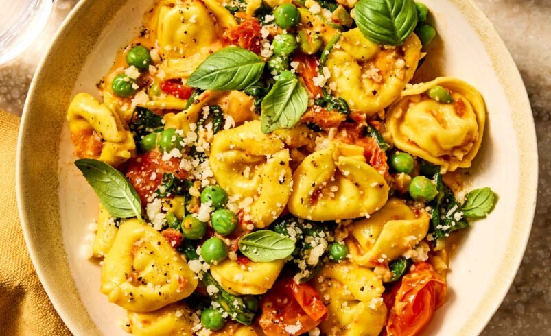 Prato de tortellini coberto com ervilhas, tomate cereja e folhas de manjericão.