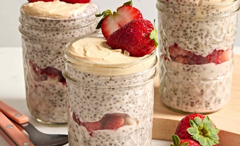 Três potes de vidro com pudim de chia, morangos frescos e colheres ao lado.